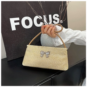 Detail of light yellow straw shoulder bag with silver metal bow and leather handle