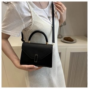 Detail of black lizard-embossed faux leather handbag with elegant gold metal buckle