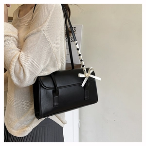 Detail view of black ballet-style baguette bag with woven bow ribbon on shoulder strap