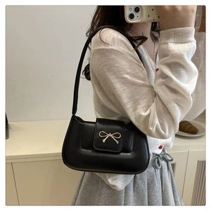 Détail d'un sac baguette noir avec une élégante décoration de nœud en métal doré