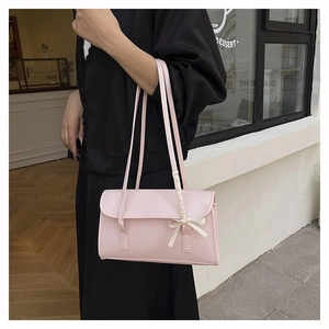Detail of pink shoulder bag with bow and woven trim on a model in a cafe setting