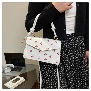 Detail of white cherry crossbody bag with knot handle and gold hardware detail