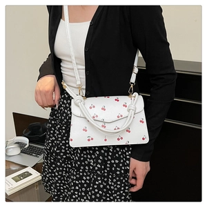 Detail of white leather crossbody bag with cherry prints and slim shoulder strap