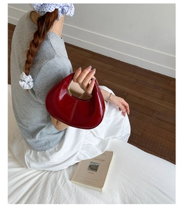 Sac hobo rouge en cuir verni brillant tenu par un mannequin dans un décor épuré