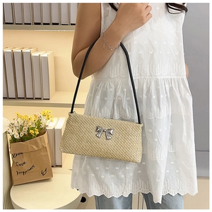 Detail of woven straw bucket bag with silver bow accent and slim black shoulder strap