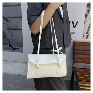Sac à bandoulière crème avec nœud porté par un mannequin dans un décor urbain chic
