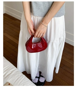 Vue de dessus d'un mini sac demi-lune rouge brillant sur robe blanche et parquet