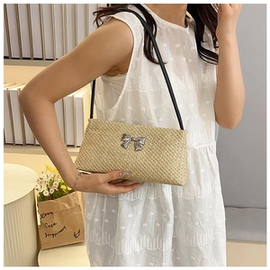 Detail of straw shoulder bag with silver metal bow and black leather strap on white lace dress