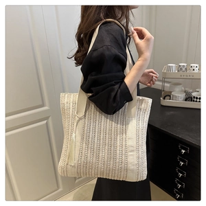 Detail of woven straw tote bag featuring creamy canvas straps and white fringe tassel