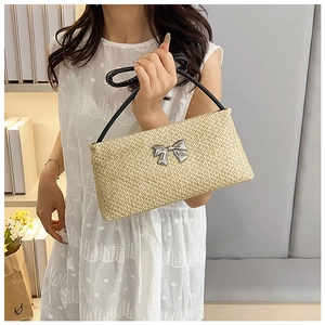 Detail of straw woven bag with black ring handle and silver bow metal accessory
