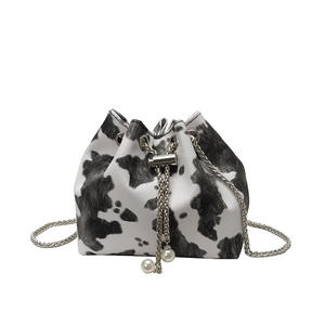 Cow print bucket bag with silver chain strap and pearl drawstring on white background