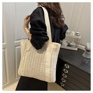 Detail of light beige woven tote bag featuring a tassel and wide shoulder strap