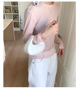 Detail of a white glossy crescent hobo bag with sleek metal clasp shown in a chic interior