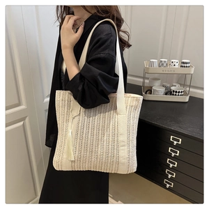 Detail of cream woven straw tote bag featuring decorative tassels and soft shoulder straps