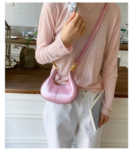 Detail of pink crescent bag with glossy finish and gold metal buckle on shoulder strap