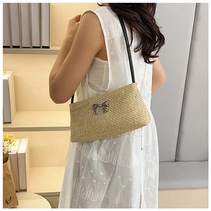 Detail of light khaki straw shoulder bag with silver bow accent and slim black strap