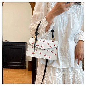 Close-up of stylish white crossbody bag with red cherry prints and knot handle