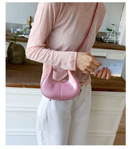 Detail of light pink patent leather crescent bag with decorative stitching and slim strap