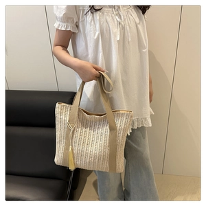 Detail of hollow woven straw beach tote bag with yellow tassel and wide textile straps