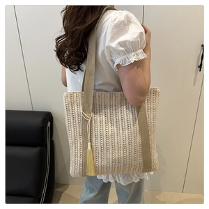 Close-up of woven tote bag featuring beige stripes, yellow silk tassel, and wide fabric straps