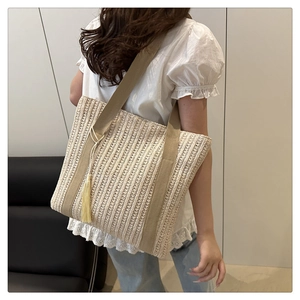 Detail of woven straw tote bag with brown fabric handles and long tassel decoration