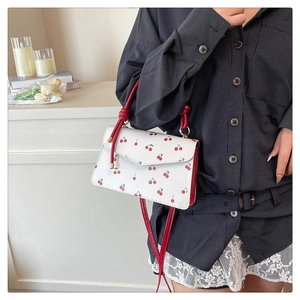 Détail du sac à main blanc à motif cerise avec poignée rouge et nœud dans un décor intérieur