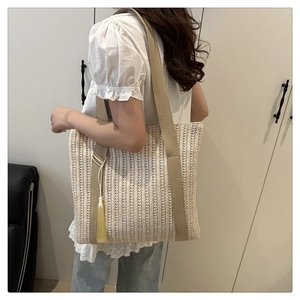Close-up of beige woven straw tote bag featuring a khaki fabric strap and yellow silk tassel