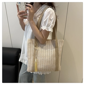 Detailed texture of hand-woven straw tote bag with yellow tassel and canvas strap