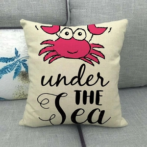 Linen square pillow with pink crab design and 'Under The Sea' text on a gray sofa