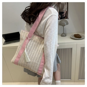 Detail view of woven straw tote bag with pink canvas handles and white tassel charm