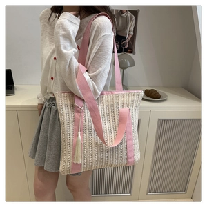 Detail of hollow woven tote bag featuring pink wide straps and a white tassel charm