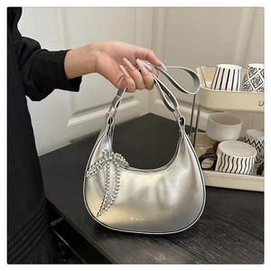 Close-up of metallic silver crescent bag featuring a pearl bow charm and fashion logo