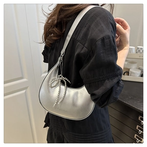 Detail of silver crescent shoulder bag with beaded bow charm and fashion logo print