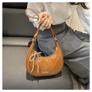 Detail of caramel crescent shoulder bag with glossy finish and silver beaded bow charm