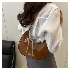 Detail of a brown crescent bag with beaded bow charm and Fashion print on sleek leather