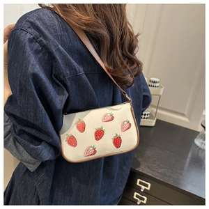 Detailed view of white shoulder bag with strawberry print and brown strap in home setting