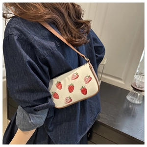 Close-up of strawberry print tote bag with brown leather strap worn on shoulder