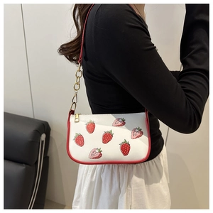 White shoulder bag with red strawberry pattern and gold chain strap shown on a model