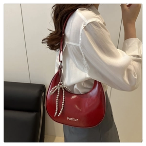 Close-up of a red glossy crescent shoulder bag featuring a silver beaded bow detail