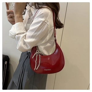Détail du sac demi-lune en cuir brillant rouge avec charm nœud argenté et logo