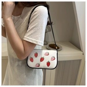 Close-up of a white strawberry print shoulder bag with black strap and leather texture