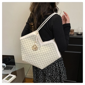 Detail of a cream tote bag with letter print, golden M charm, and spacious interior