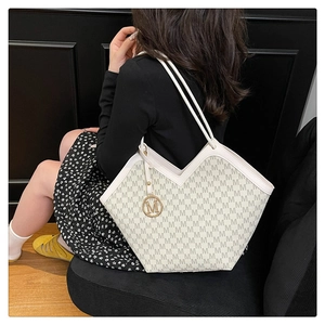 Close-up of white bucket bag with all-over M-letter print and gold metal pendant decoration