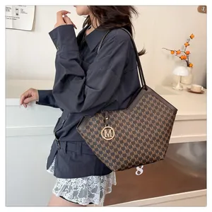 Brown monogram tote bag with letter pattern and metal charm pendant shown in lifestyle setting