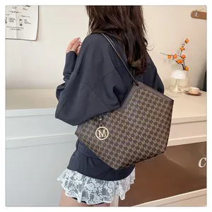 Détail de sac cabas marron avec motif de lettres et pendentif en métal M au dos