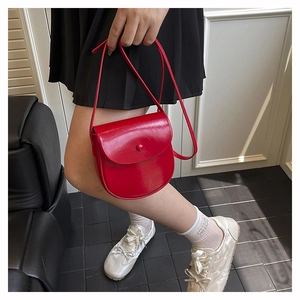 Detail of red patent leather saddle bag with round button flap and crossbody strap