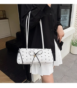 Détail du sac sous l'aisselle blanc avec motifs nœuds noirs et pendentif cœur doré