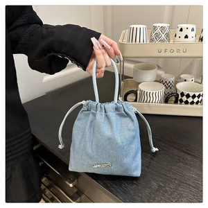 Détail du sac seau en denim bleu clair avec logo métallique JINGPIN et fermeture à cordon