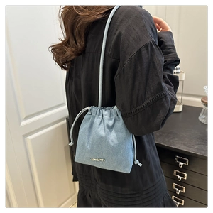 Detailed back view of a woman wearing a light blue denim textured bucket bag with metal logo