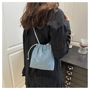 Detail of light blue denim drawstring bucket bag with JINGPIN metal plaque shown on model